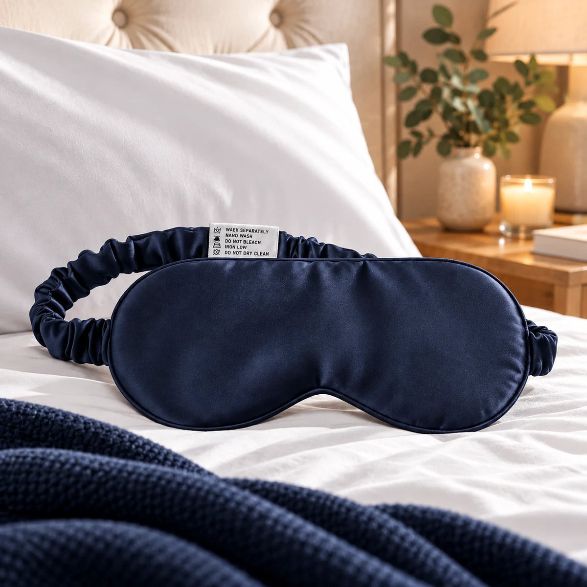 Navy bamboo lyocell sleep eye mask with adjustable strap in a bedroom lifestyle setting.