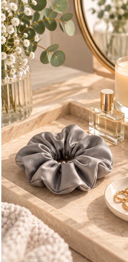 Grey bamboo lyocell hair scrunchie on a dressing table tray beside dried flowers and a perfume bottle.