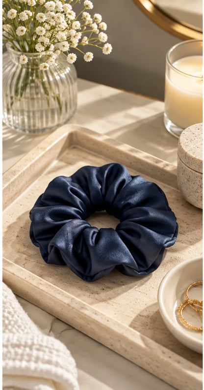 Navy bamboo lyocell hair scrunchie on a dressing table tray with dried flowers, a candle and a gold mirror.