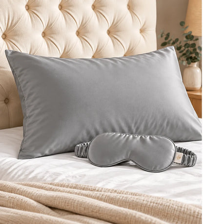 The Sleep Duo in grey: bamboo lyocell pillowcase and matching eye mask on a bed with a tufted headboard.
