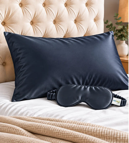 The Sleep Duo in navy: bamboo lyocell pillowcase and matching eye mask on a bed with a tufted headboard.
